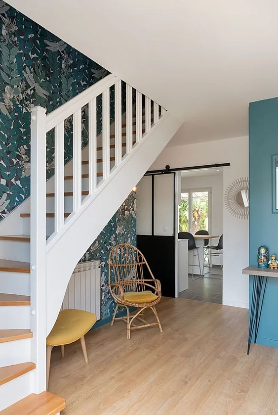 Escalier blanc et bois avec papier-peint végétal, fauteuil et radiateur dessous escalier